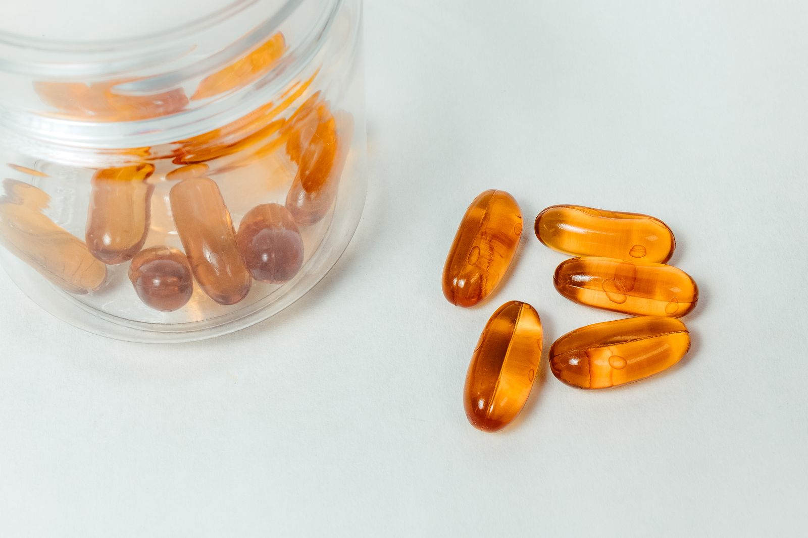 Amber softgels spilling from an open jar onto warm limestone — the studied dose, and nothing else.